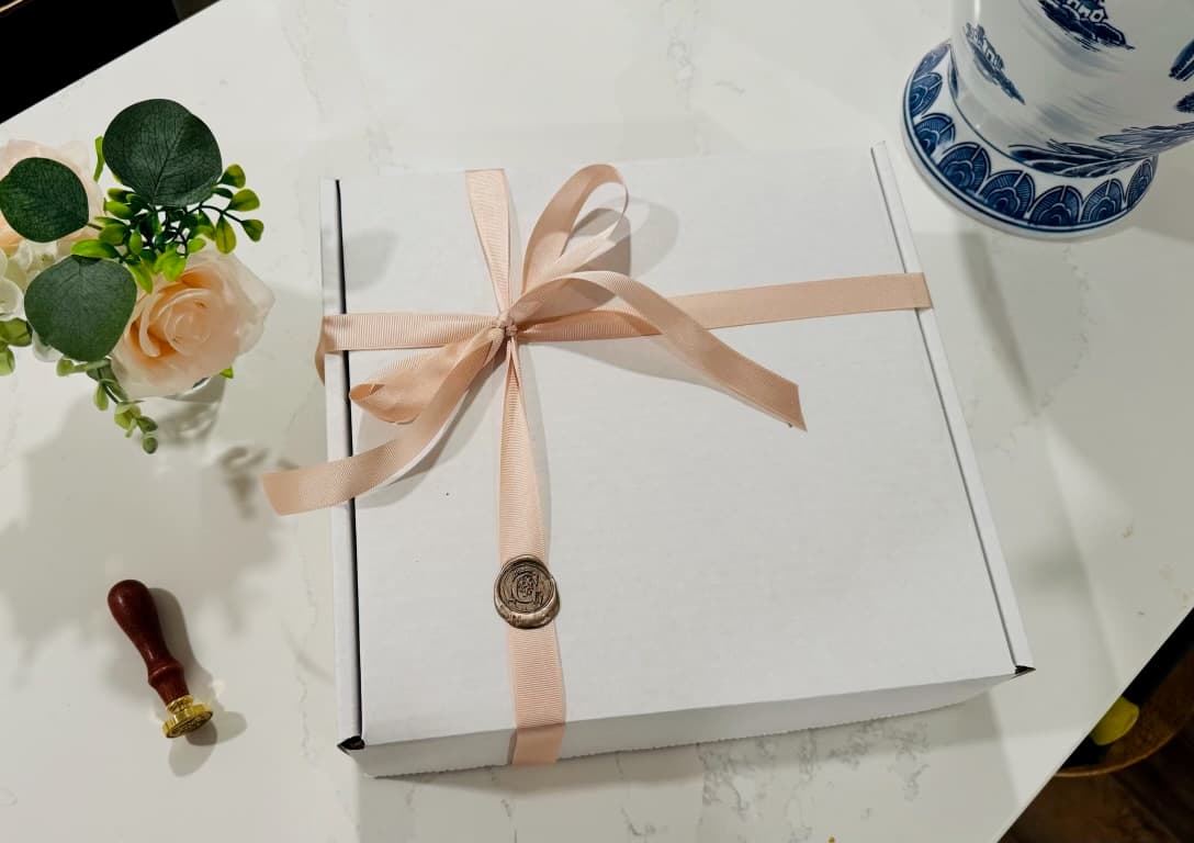 A white gift box with blush pink ribbon, gold wax seal, and hand-pressed stamp — every delivery is an occasion